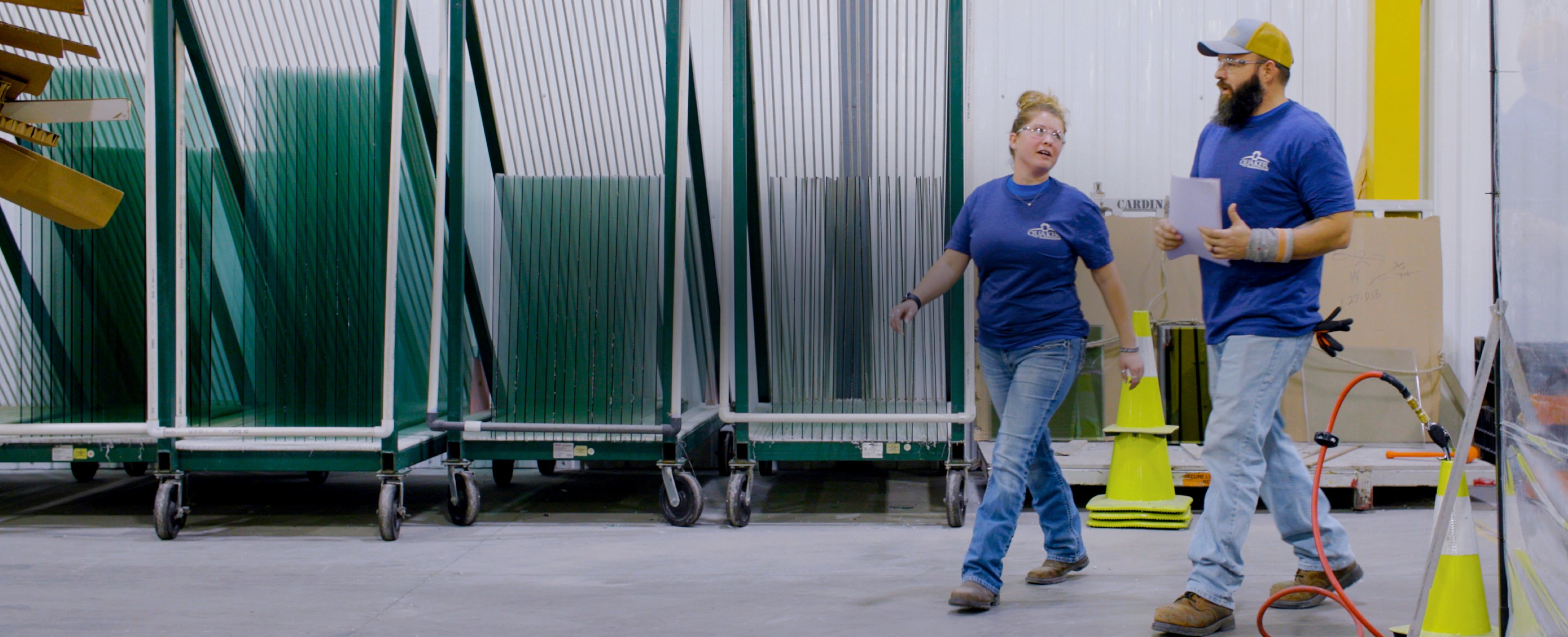 Two Quaker Windows and Doors employees working and walking in factory.